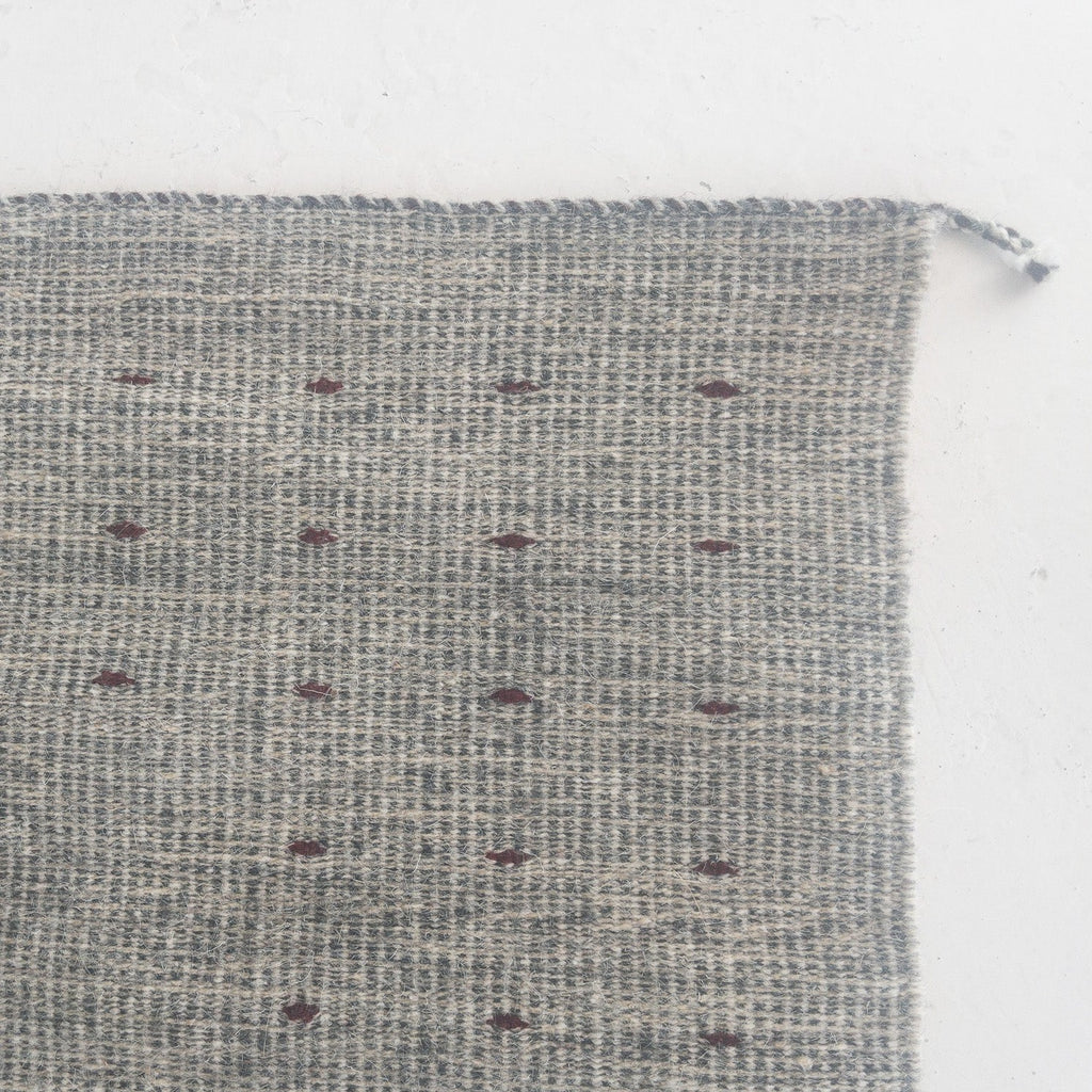 a zoomed in corner of a handmade zapotec rug with gray and maroon wool fibers