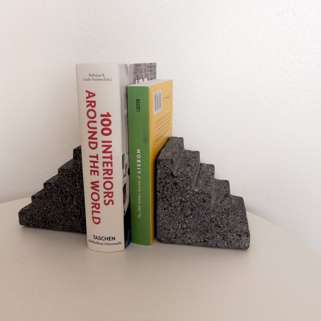 Studio CM | Bookends in the shape of a Pyramid holding two books. The book ends are made of volcanic stone and have a porous exterior.