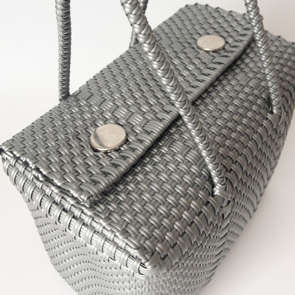 Studio CM | A hand woven silver plastic reusable purse. It is woven together with individual strands, held together by magnetic buttons and has two straps.