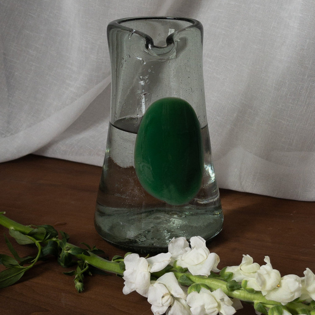 Studio CM | a clear carafe with a spout and green dot in the middle that was hand made in mexico