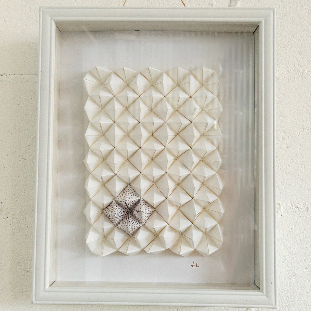 Studio CM | An abstract origami composition framed in a box that has a monotone white color with a touch of gold. Handmade pieces of origami delicately glued together.