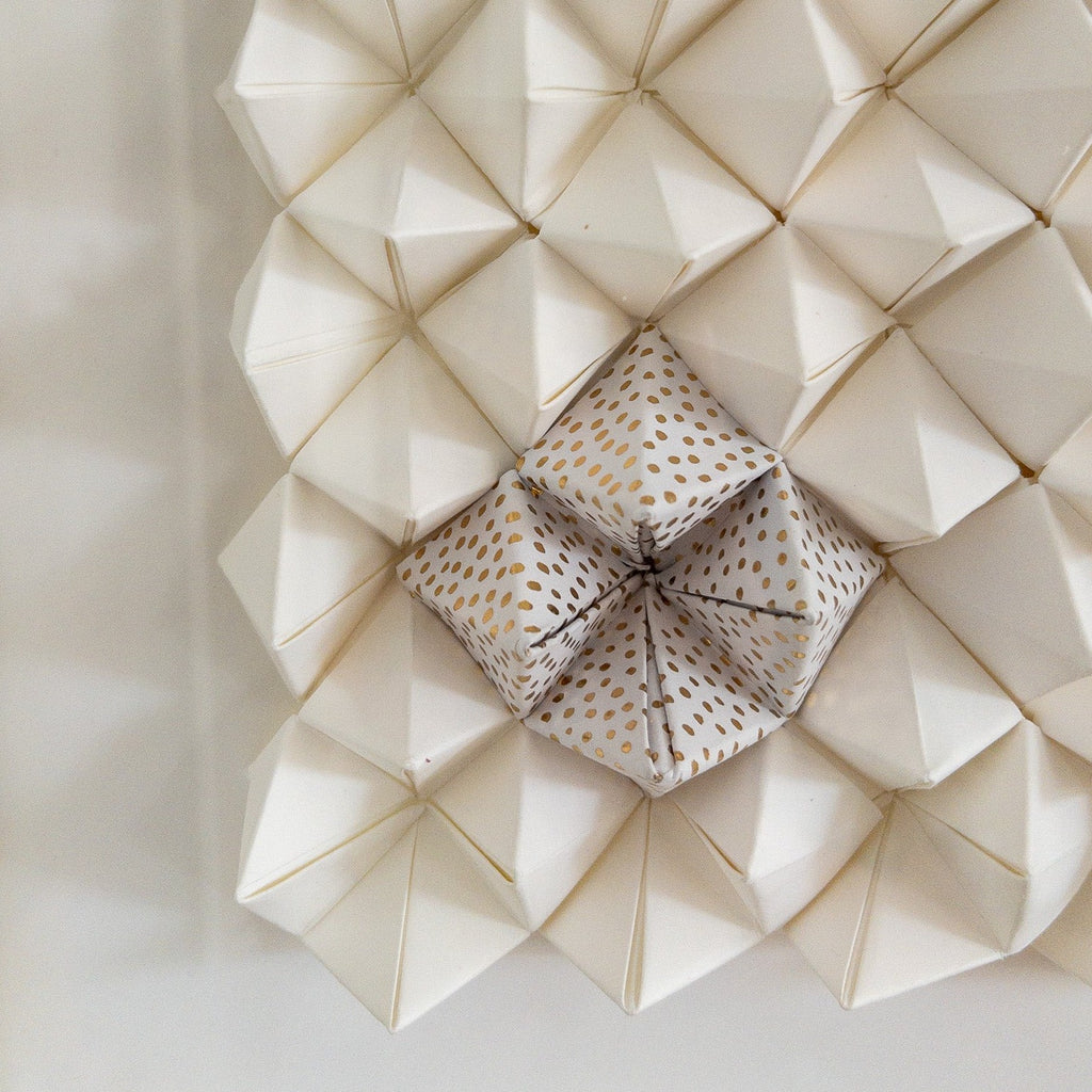 Studio CM | An abstract origami composition framed in a box that has a monotone white color with a touch of gold. Handmade pieces of origami delicately glued together.