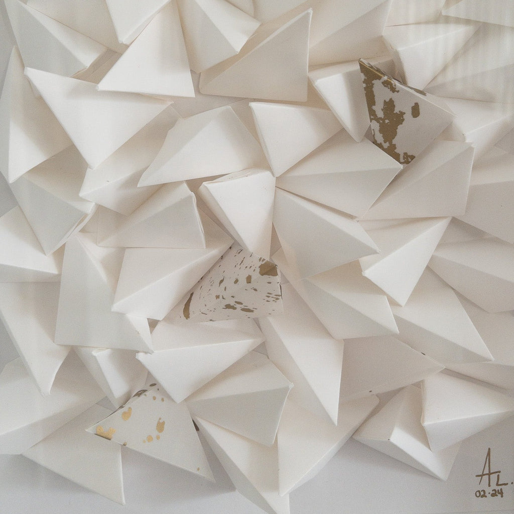 Studio CM | An abstract origami composition framed in a box that has a monotone white color with a touch of gold. Handmade pieces of origami delicately glued together. 