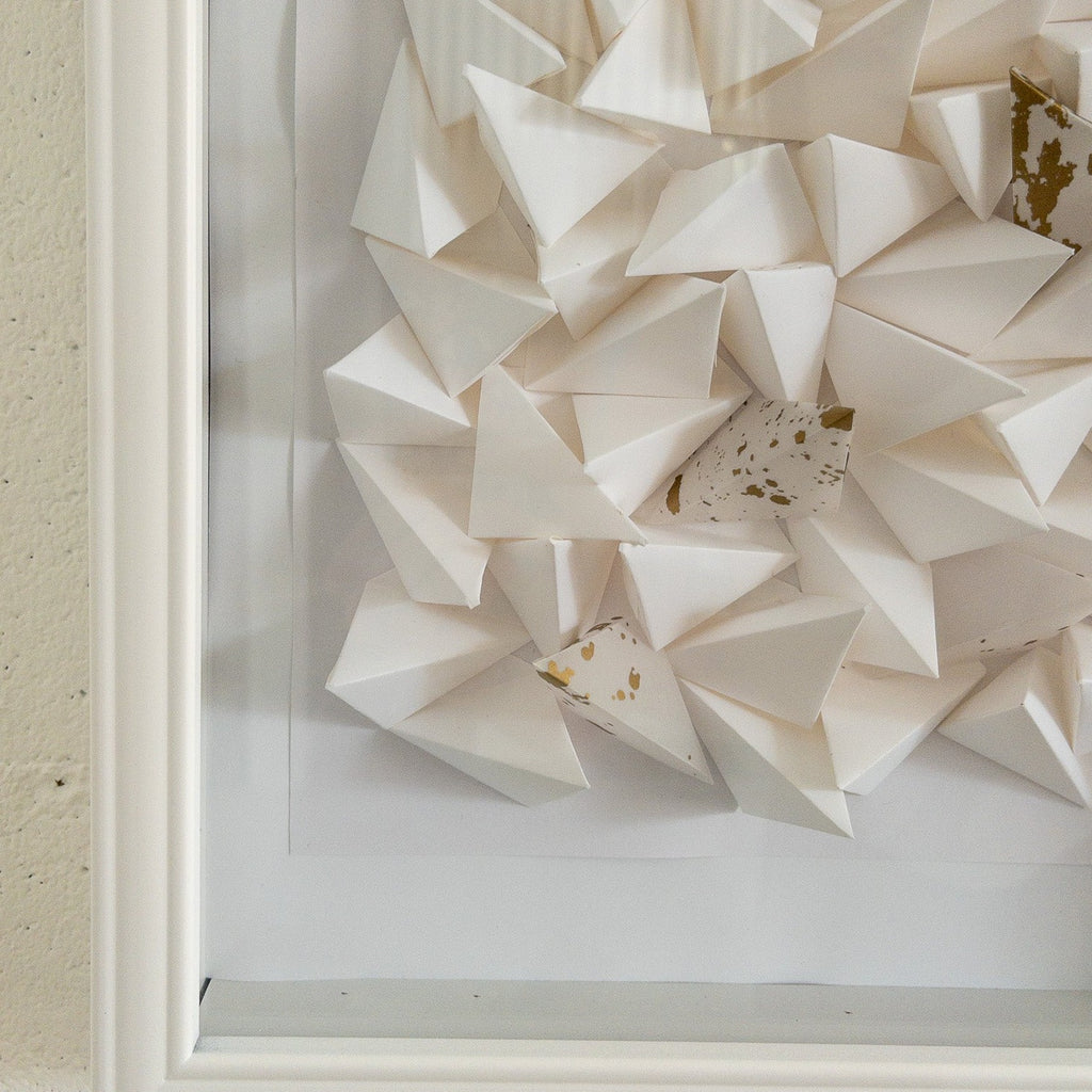 Studio CM | An abstract origami composition framed in a box that has a monotone white color with a touch of gold. Handmade pieces of origami delicately glued together. 