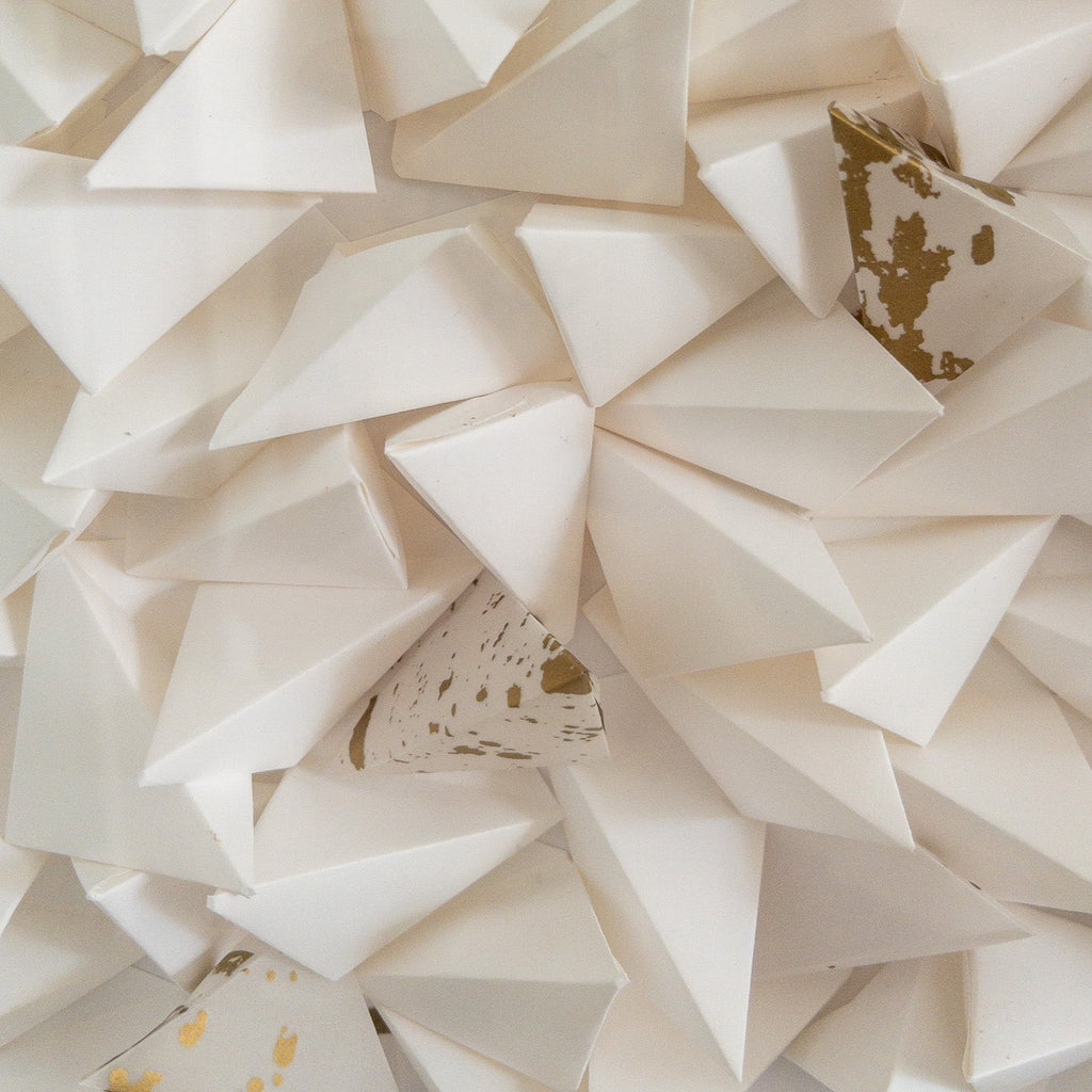 Studio CM | An abstract origami composition framed in a box that has a monotone white color with a touch of gold. Handmade pieces of origami delicately glued together. 