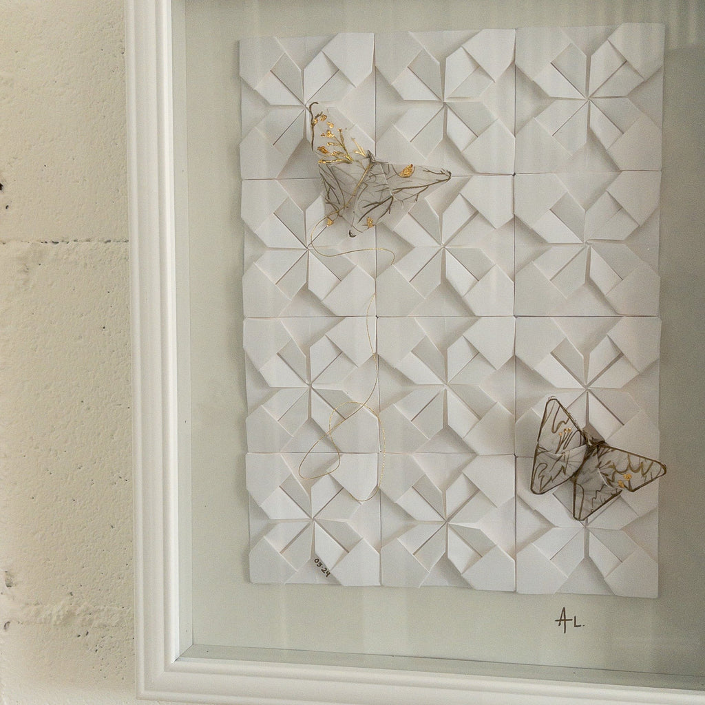 Studio CM | A framed composition made of origami. It's a wall decor piece by Alicia Lopez with white origami squares and butterflies. 