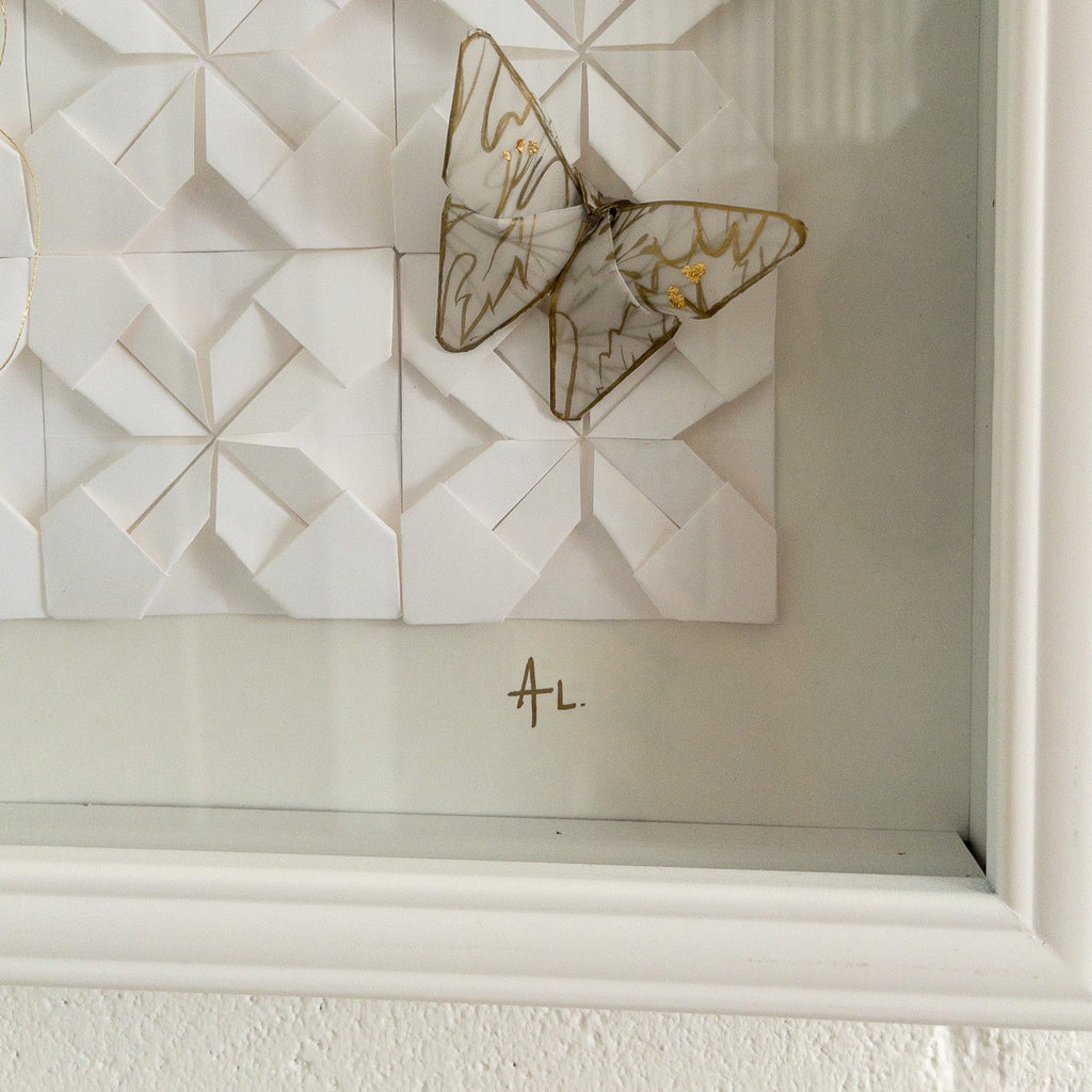 Studio CM | A framed composition made of origami. It's a wall decor piece by Alicia Lopez with white origami squares and butterflies. 