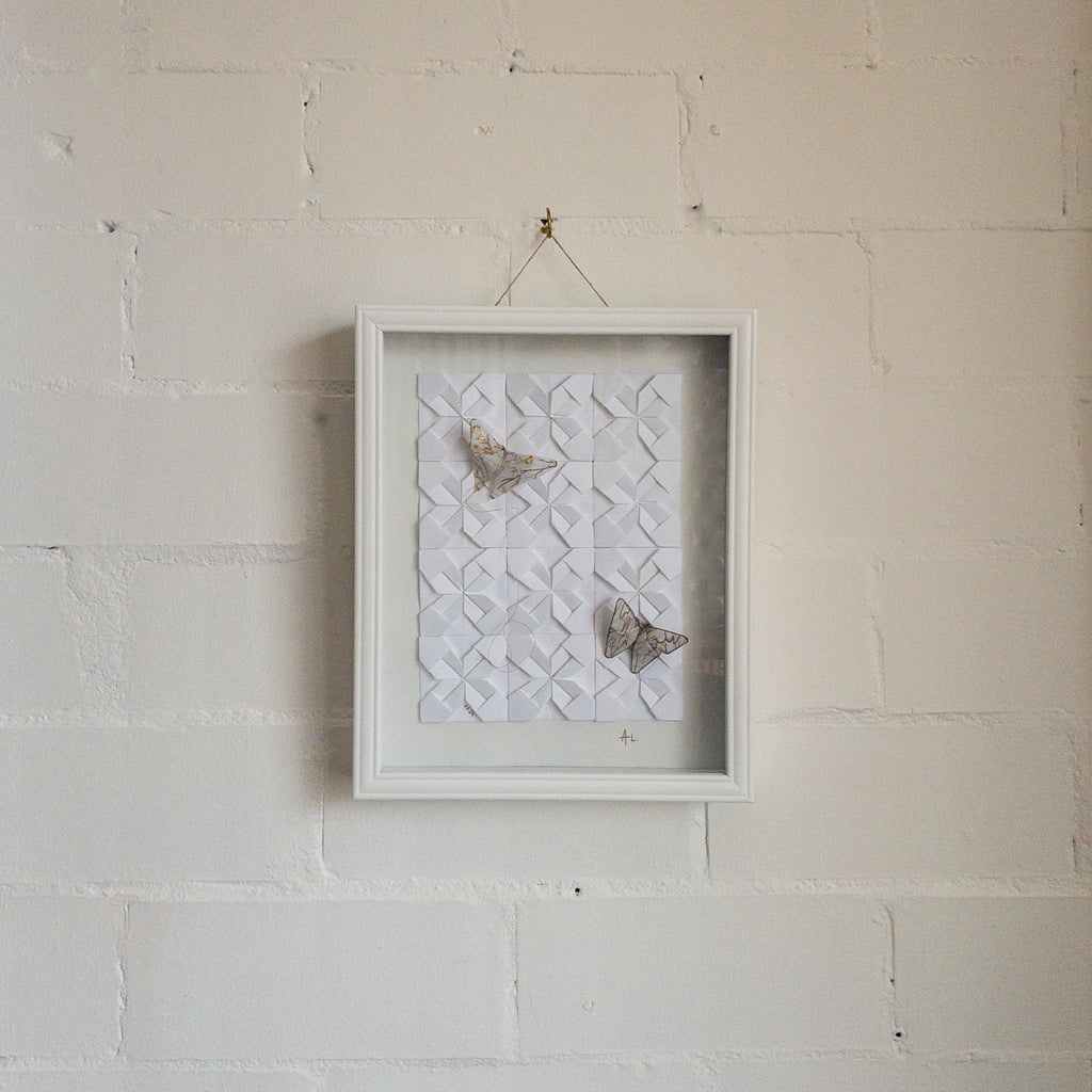 Studio CM | A framed composition made of origami. It's a wall decor piece by Alicia Lopez with white origami squares and butterflies. 