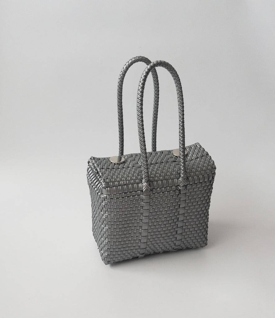 Studio CM | A hand woven silver plastic reusable purse. It is woven together with individual strands, held together by magnetic buttons and has two straps.