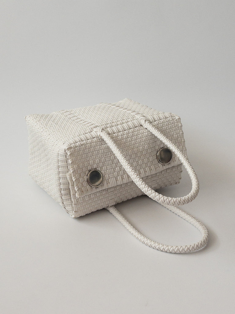 Studio CM | A hand woven white plastic reusable purse. It is woven together with individual strands, held together by magnetic buttons and has two straps.