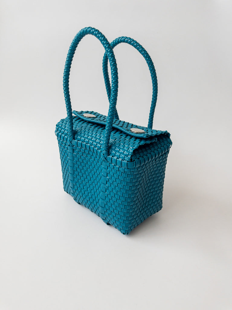 Studio CM | A hand woven teal plastic reusable purse. It is woven together with individual strands, held together by magnetic buttons and has two straps.