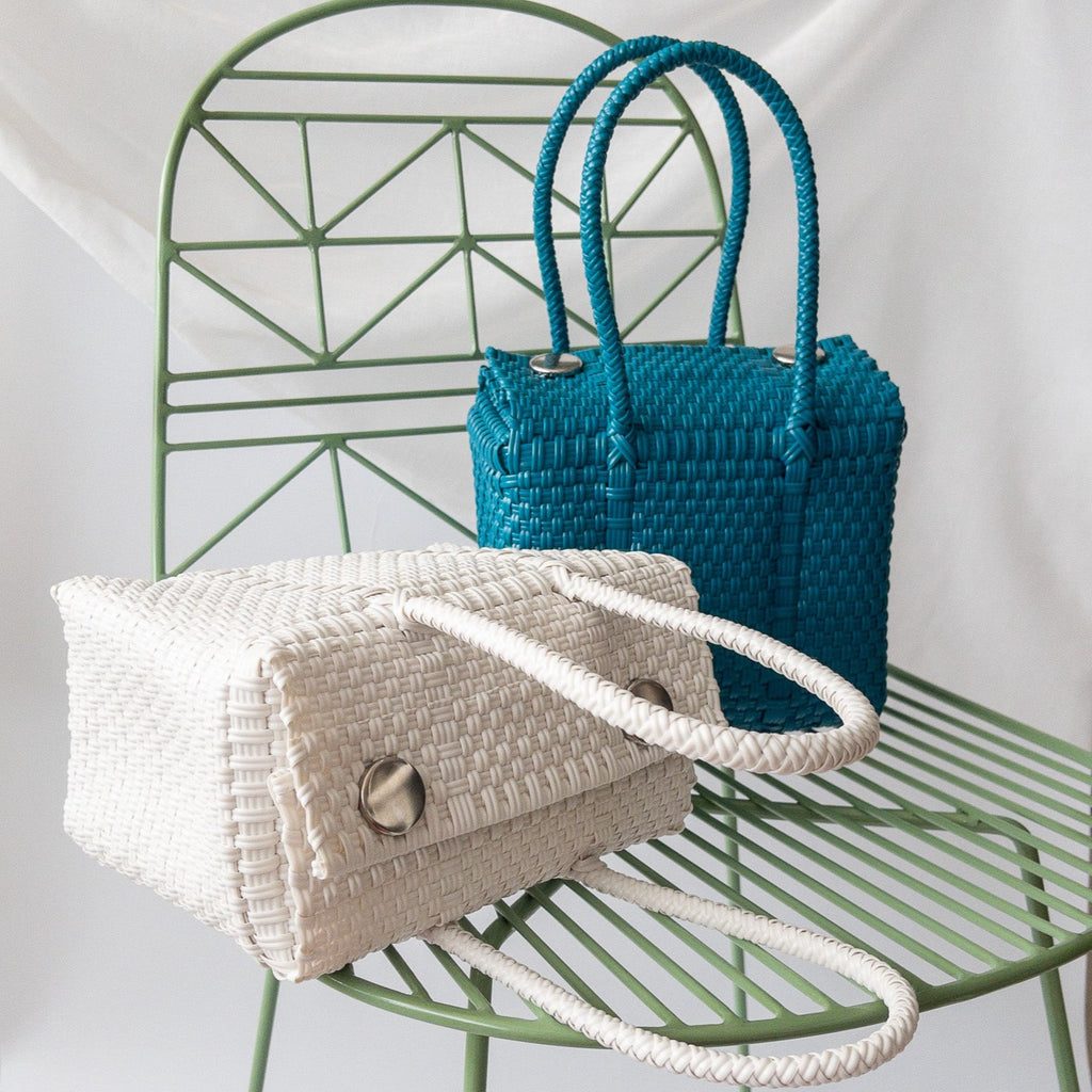 Studio CM | A hand woven white plastic reusable purse. It is woven together with individual strands, held together by magnetic buttons and has two straps.