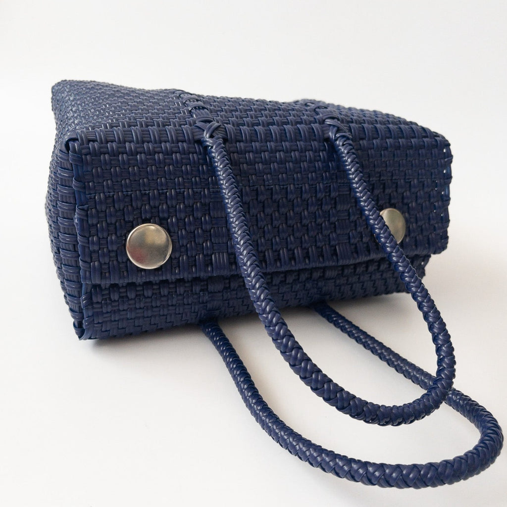 Studio CM | A hand woven navy blue plastic reusable purse. It is woven together with individual strands, held together by magnetic buttons and has two straps.