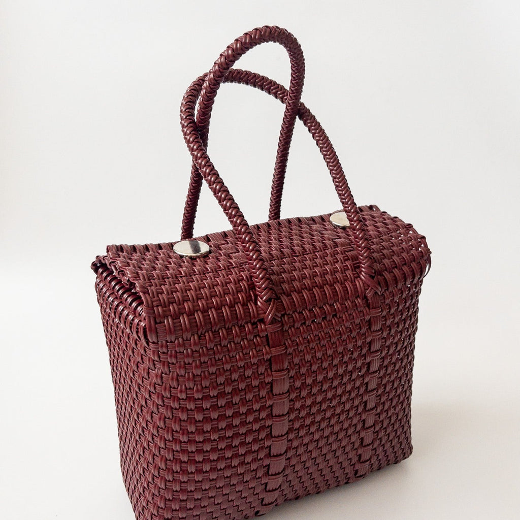 Studio CM | A hand woven maroon plastic reusable purse. It is woven together with individual strands, held together by magnetic buttons and has two straps.