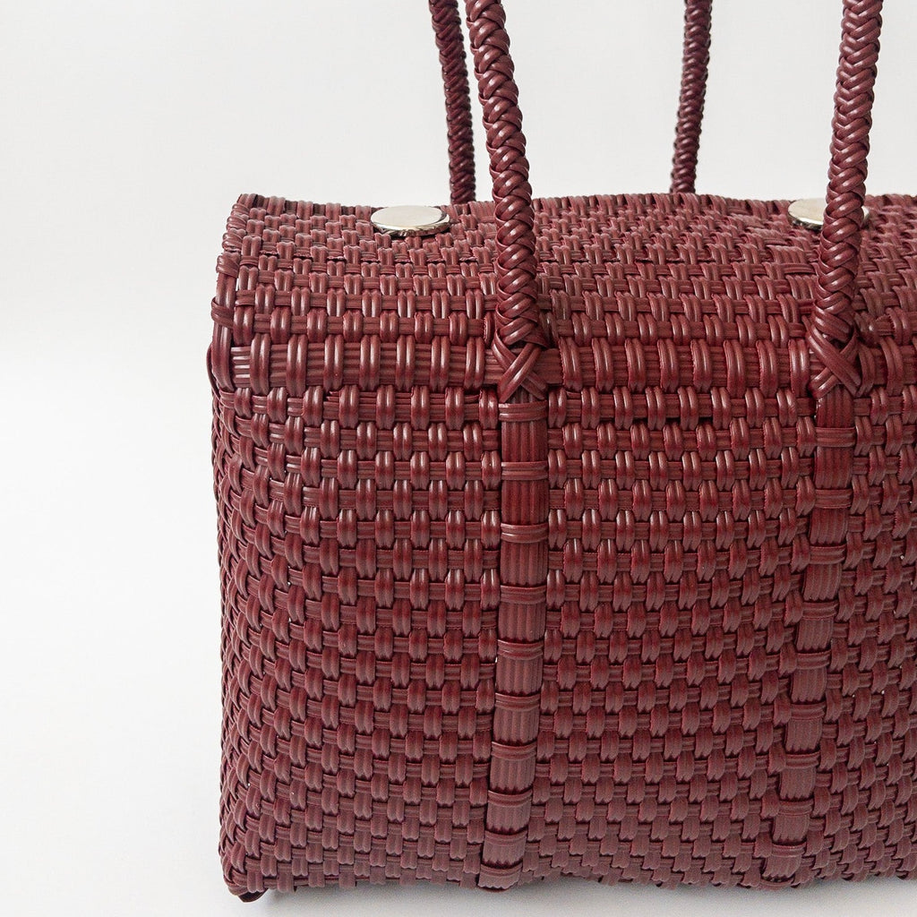 Studio CM | A hand woven maroon plastic reusable purse. It is woven together with individual strands, held together by magnetic buttons and has two straps.