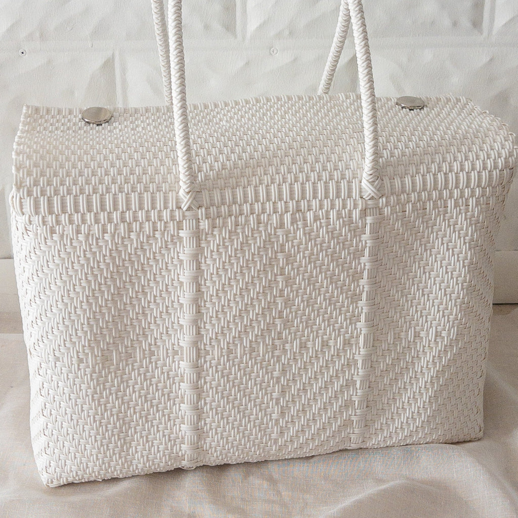 Studio CM | A white hand woven duffel with two long straps and silver buttons to clasp it shut. 