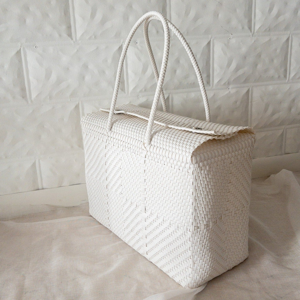 Studio CM | A white hand woven duffel with two long straps and silver buttons to clasp it shut. 