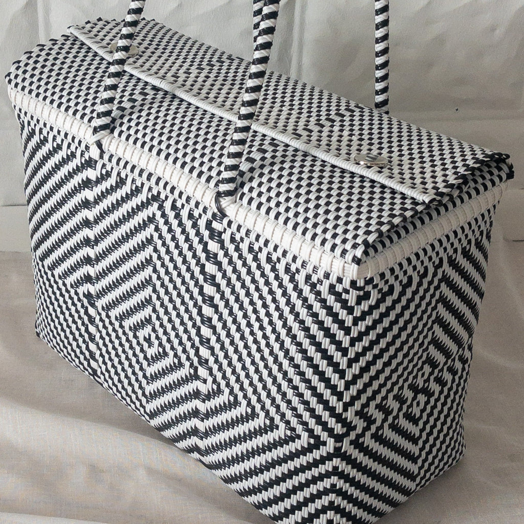 Studio CM | A black and white hand woven duffel with two long straps and silver buttons to clasp it shut. 