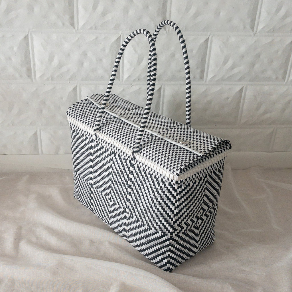 Studio CM | A white and black hand woven duffel with two long straps and silver buttons to clasp it shut. 