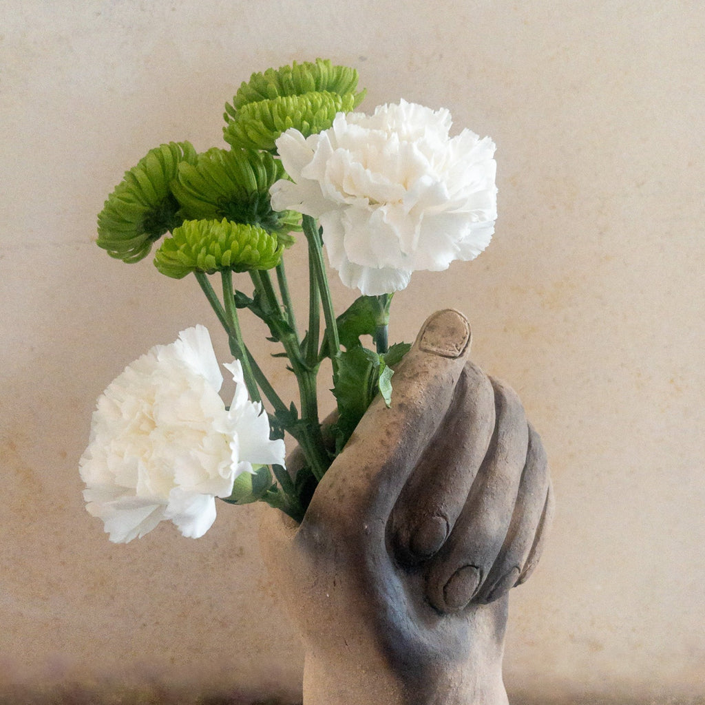 Studio CM | a sculpture that serves as a vase hand made from ceramic that is in the shape of a hand grasping flowers