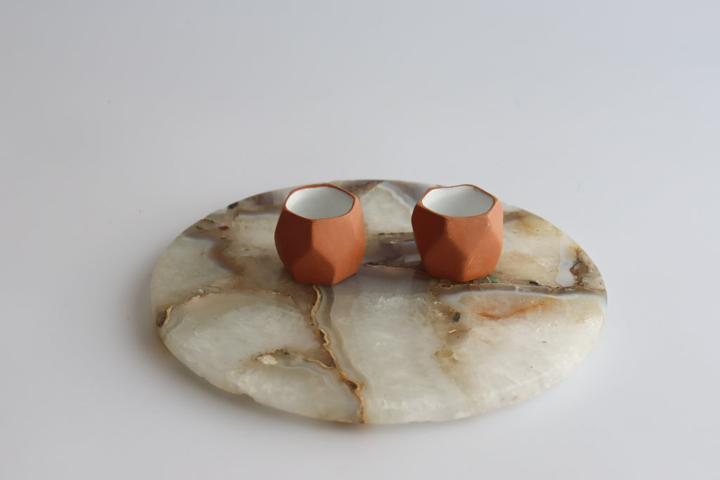 two ceramic shot glasses with white interior glaze on a round marble slab