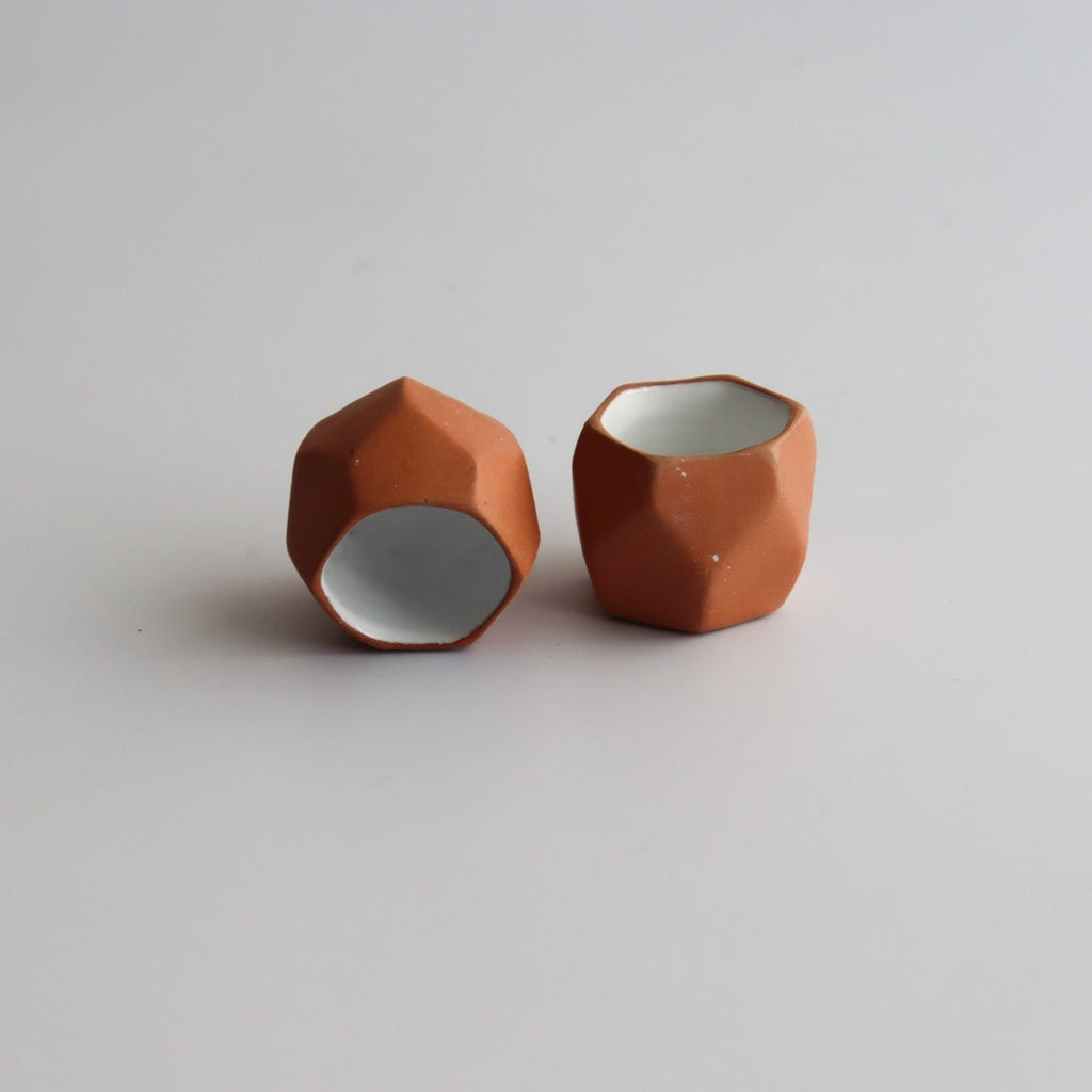 two geometric shaped traditional mexican shot glasses made of clay with a white interior glaze on a white background