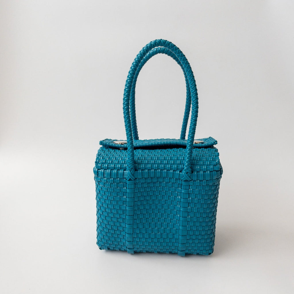 Studio CM | A hand woven teal plastic reusable purse. It is woven together with individual strands, held together by magnetic buttons and has two straps.