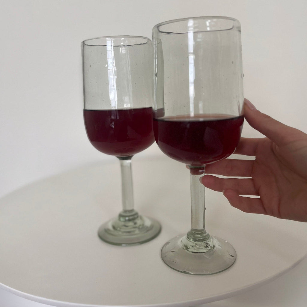 Studio CM | Two wine glasses with red liquid on a white surface, one held by a hand.