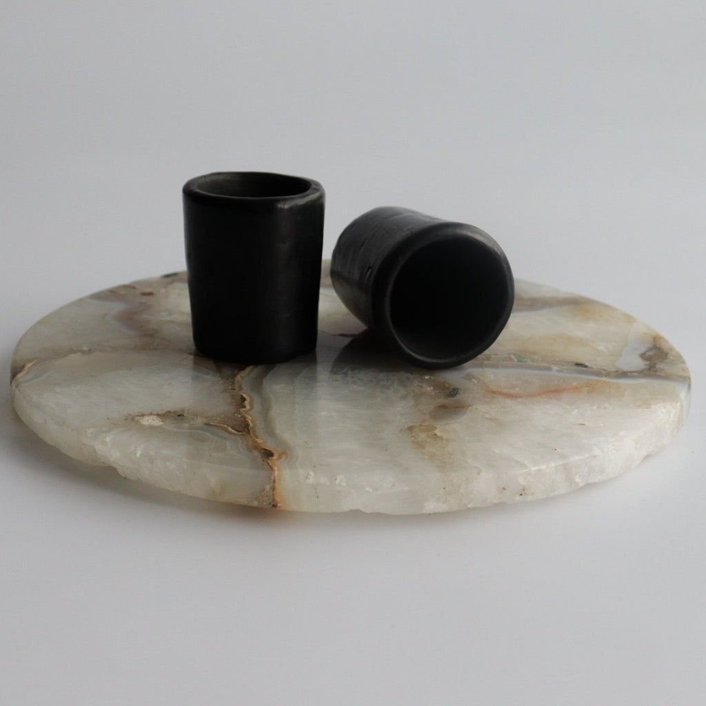 Studio CM | two black ceramic shot glasses on a marble circular slab on a white background