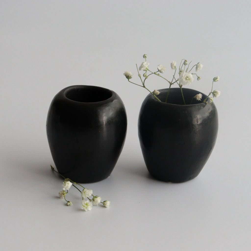 two black ceramic shot glasses with decorative white flowers and a white background