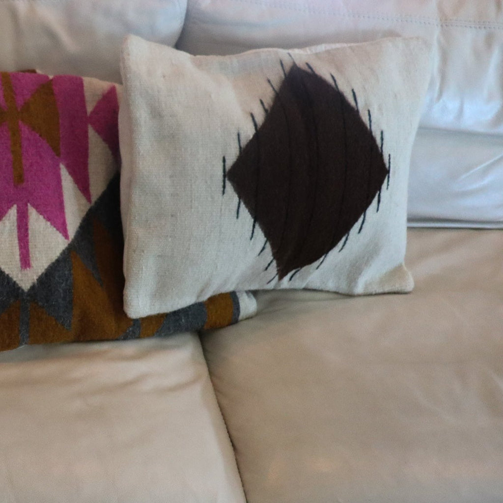 two wool handmade pillows with differing contemporary patterns on a cream colored leather coach