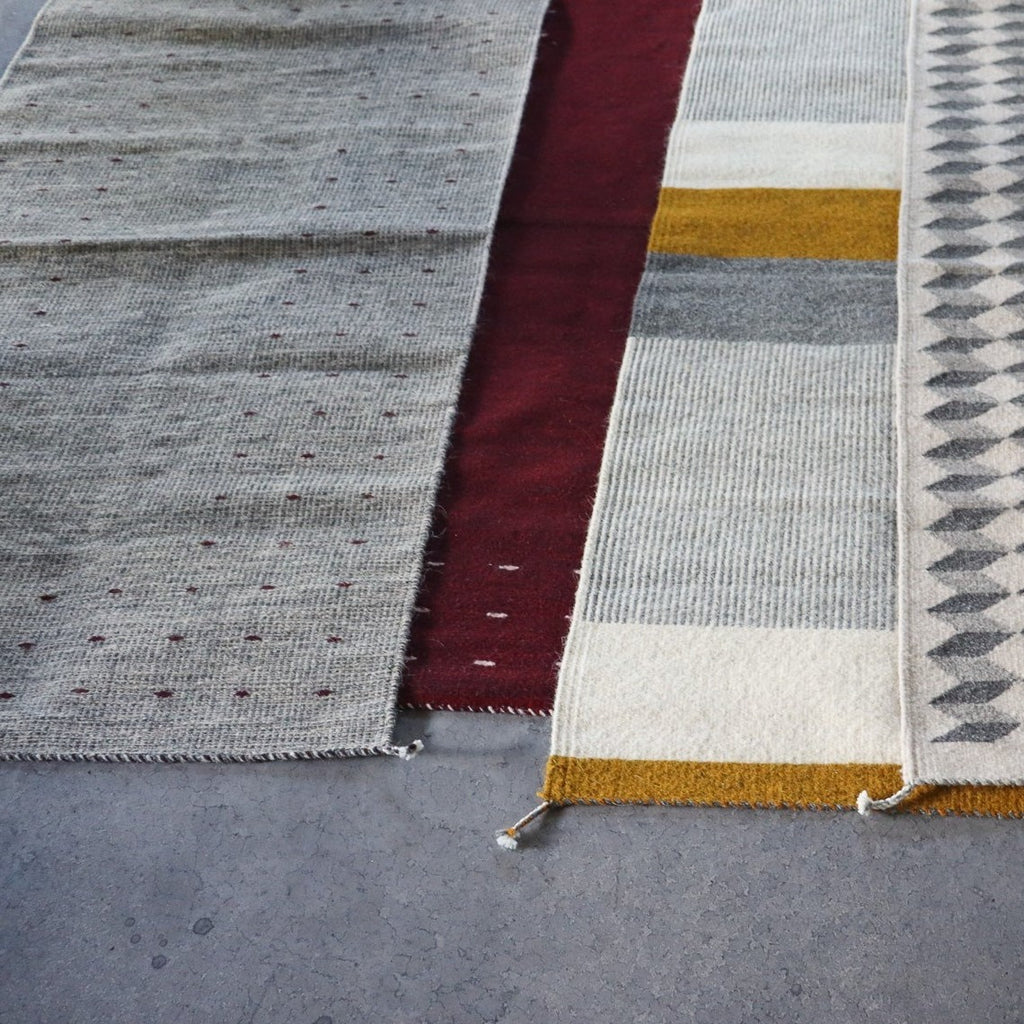 four different handmade zapotec rugs with different colors and patterns on a cement floor