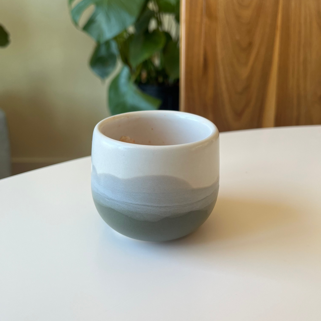Studio CM | Ceramic cup with two-tone design on a white surface with a blurred plant in the background