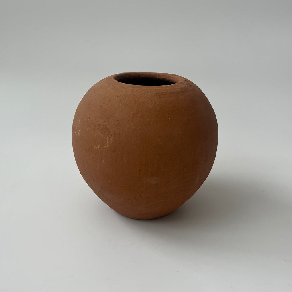 Studio CM | A terracotta planter that is round with a small plate underneath