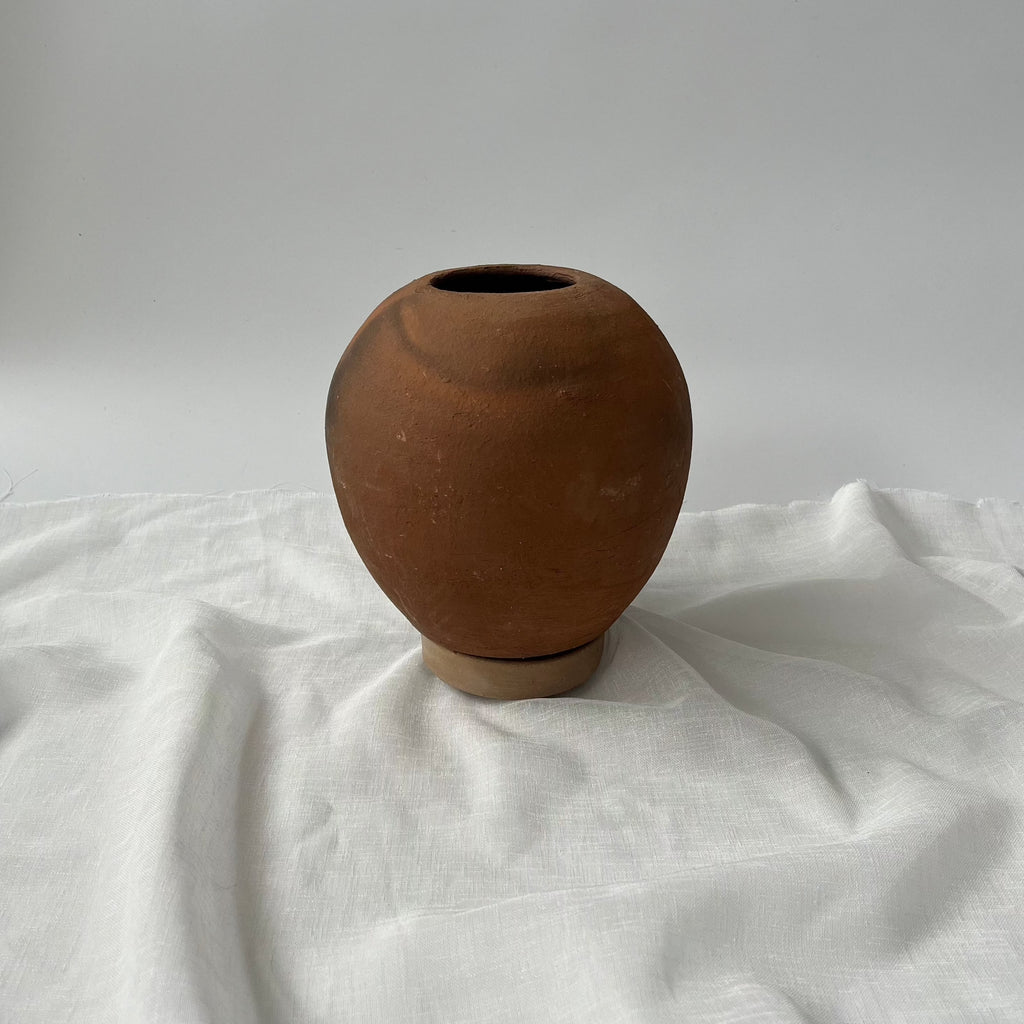 Studio CM | A terracotta planter that is round with a small plate underneath