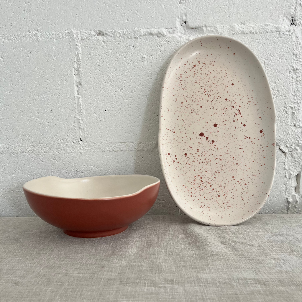 Studio CM | A terracotta ceramic bowl next to a white plate with speckles that match the terracotta bowl