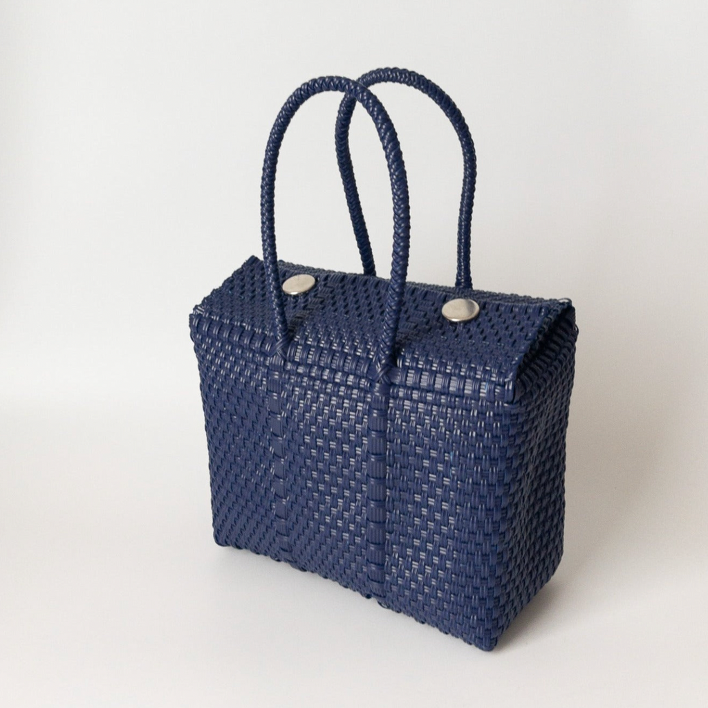 Studio CM | A hand woven navy blue plastic reusable purse. It is woven together with individual strands, held together by magnetic buttons and has two straps.