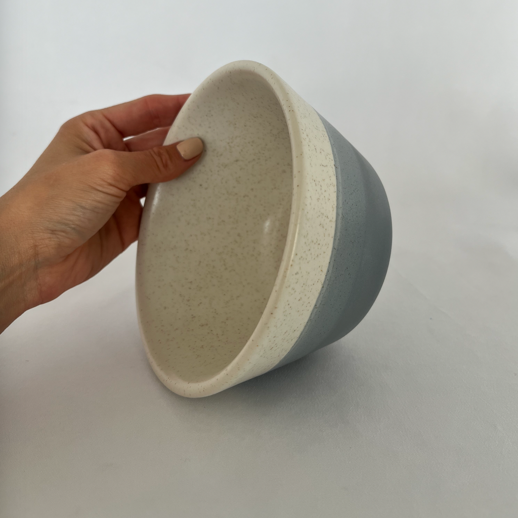 Studio CM | A handmade bowl with a speckled cream base and the bottom has wave colors of blue