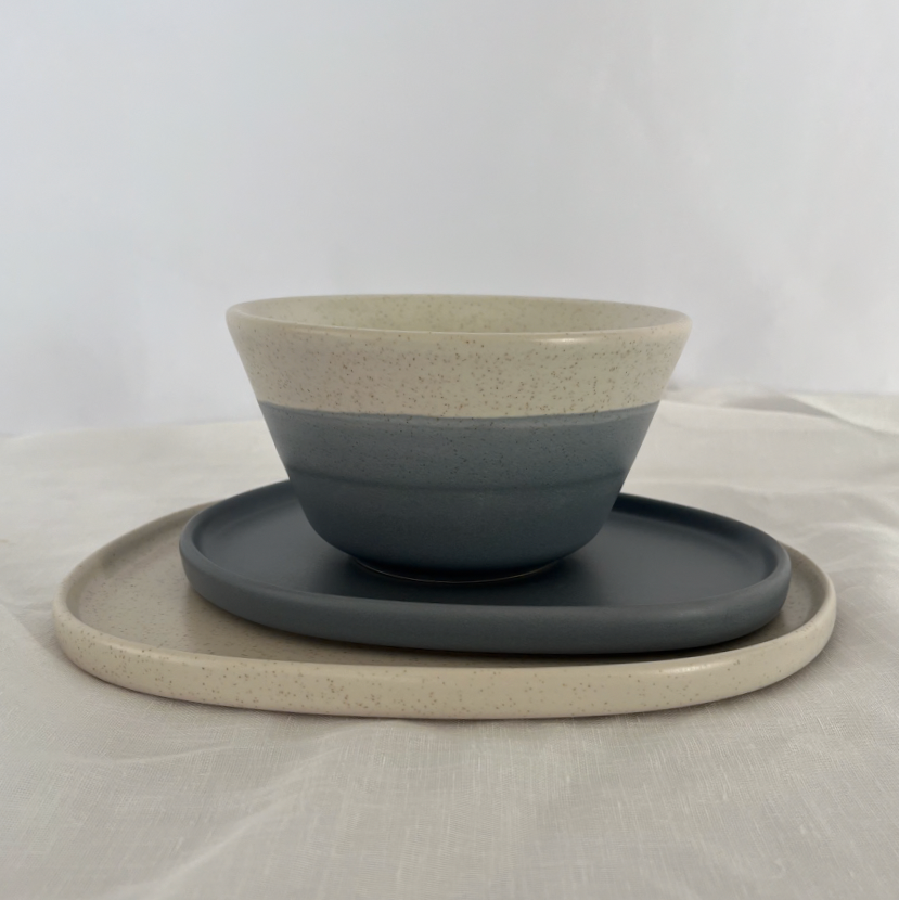 Studio CM | A handmade bowl with a speckled cream base and the bottom has wave colors of blue