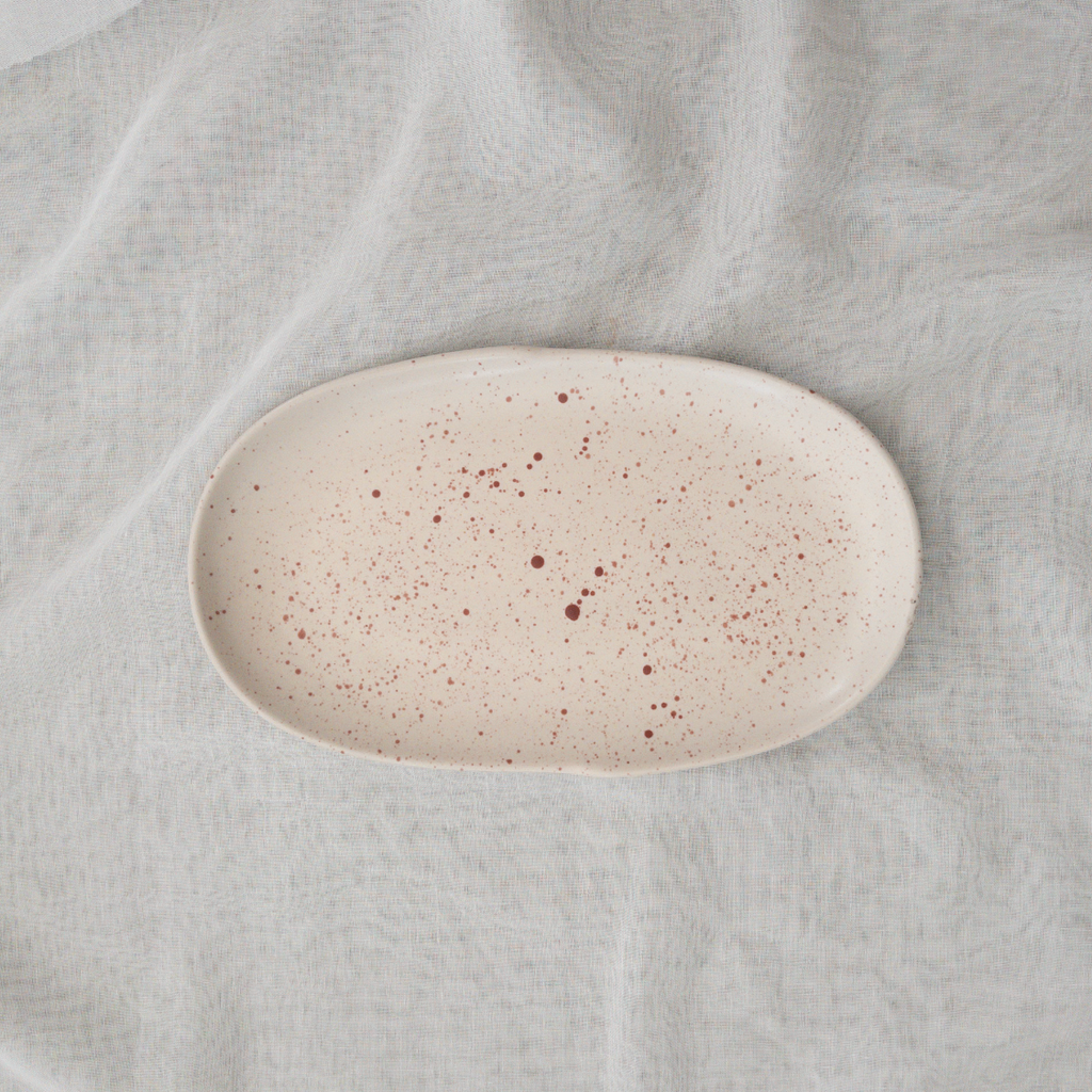 Studio CM | The top part of a ceramic plate that is a long oval shape in cream with terracotta speckles