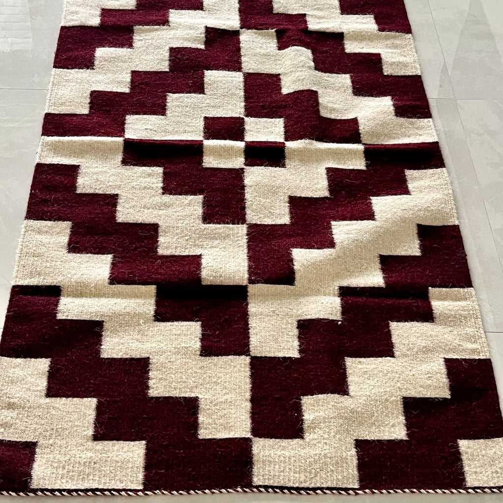 Studio CM | A maroon and cream rug with a modern geometric shape that is handwoven wool from Oaxaca Mexico