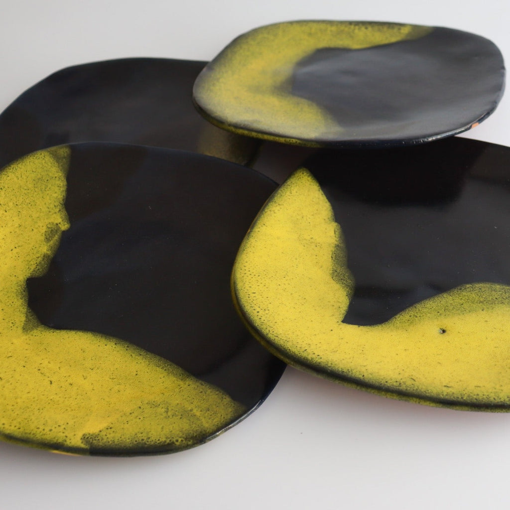 zoomed in picture of four stacked handmade ceramic plates that have blue and yellow glaze