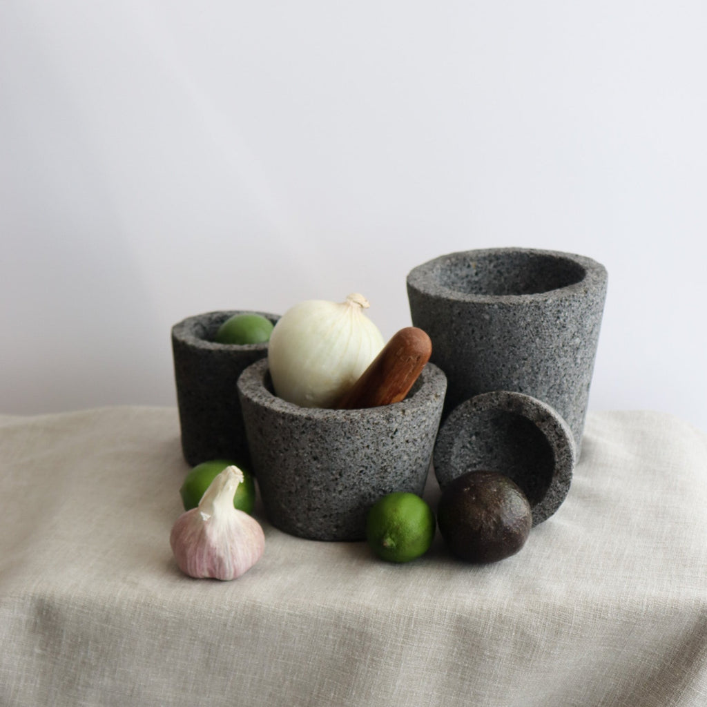 Studio CM | four volcanic stone mortars in different sizes decorated with a pestle onion garlic limes and avocado over a beige linen cloth