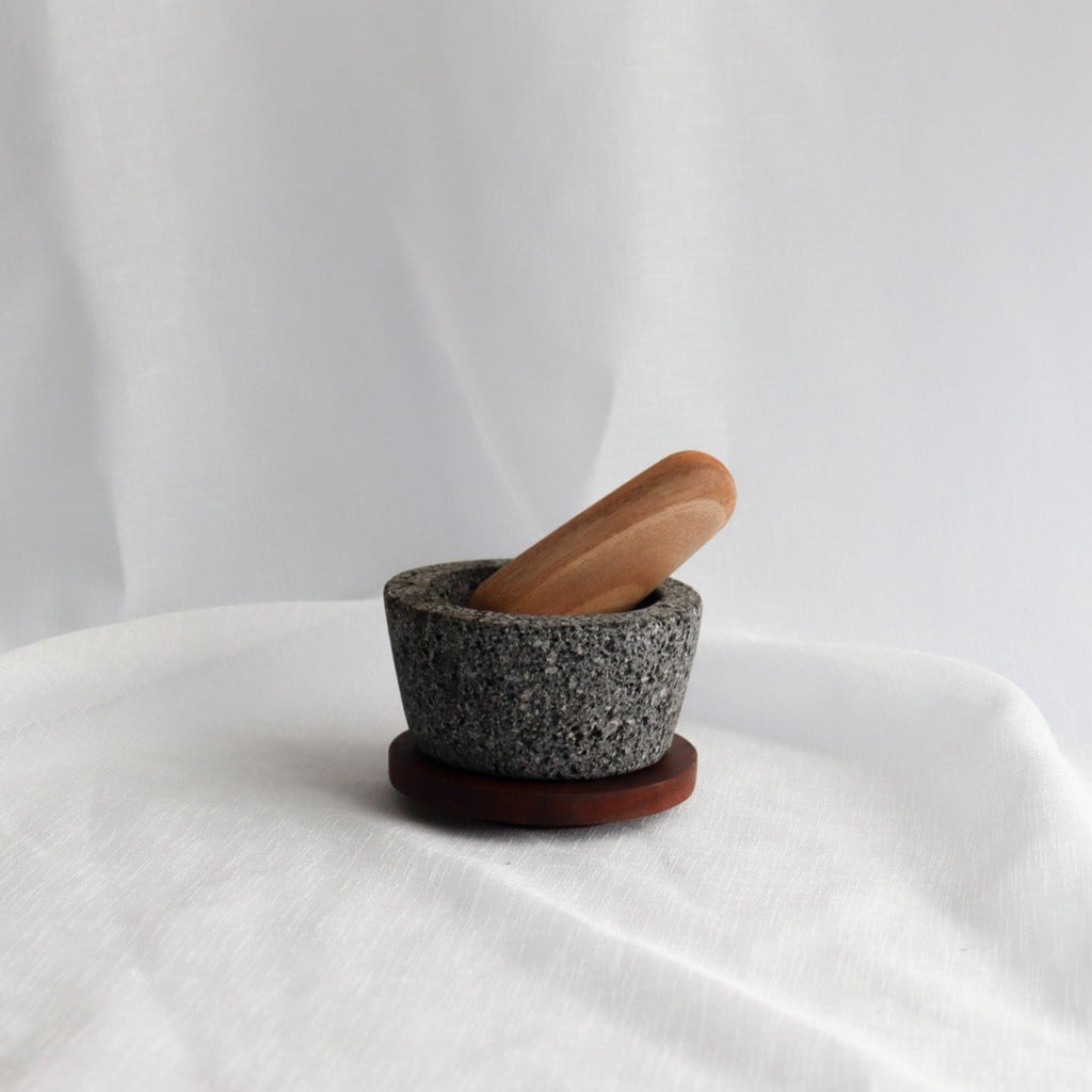 Studio CM | a small wooden handcrafted pestle inside a volcanic stone mortar on a white linen background