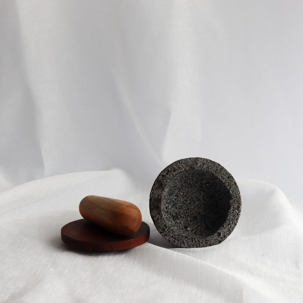 Studio CM | a small hand carved volcanic stone mortar on it's side displaying it's interior next to it's wooden top and pestle