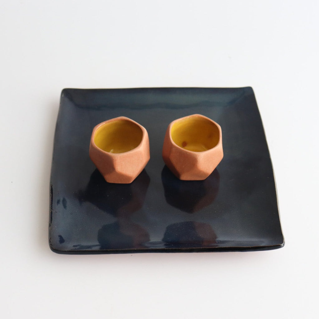 handcrafted ceramic shot glasses on a blue ceramic square plate