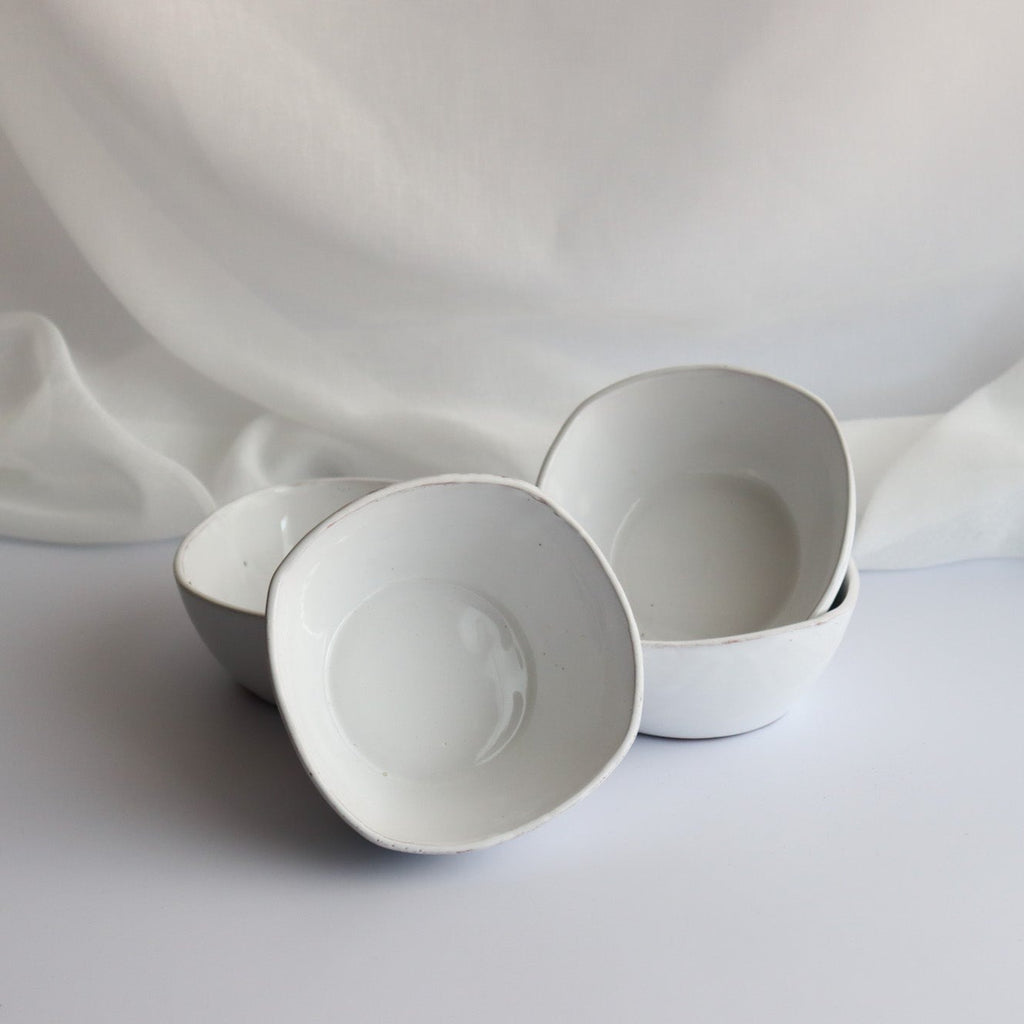 four handmade white ceramic bowls with a white linen background